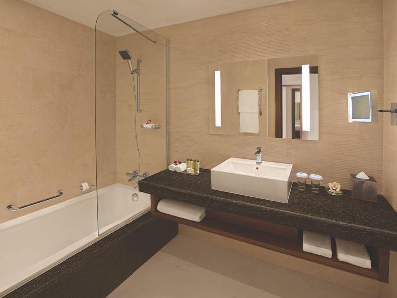 Modernes Badezimmer mit beiger Wand, Badewanne, Glasdusche, weißem Waschbecken und großem Spiegel.