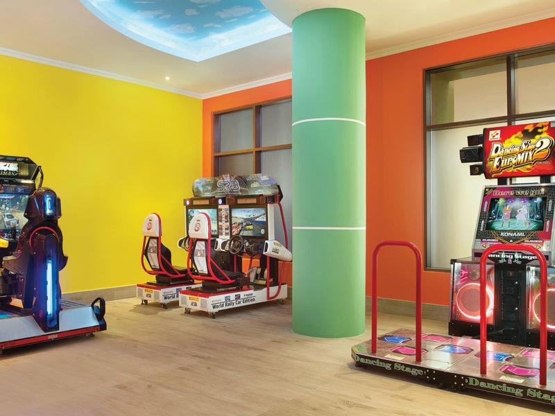 Spielautomaten mit bunten Lichtern stehen in einem hellen Raum mit gelben Wänden und grünem Säulensäule.