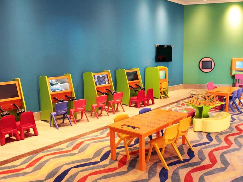 Buntes Kinderzimmer mit bunten Stühlen, Tischen, Spielkonsolen und welligem Teppichboden.