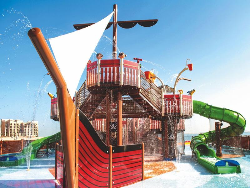 Wasserspielplatz mit einem großen Piratenschiff, Wasserrutschen und blauem Himmel im Hintergrund.