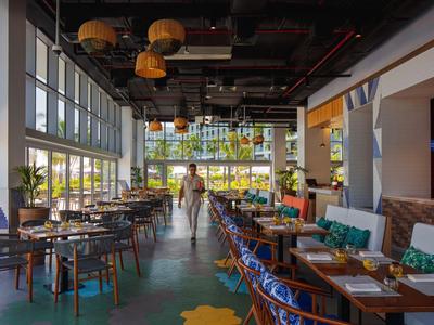 Restaurante moderno y luminoso con grandes ventanas, plantas y zonas de asiento, ideal para huéspedes del hotel.