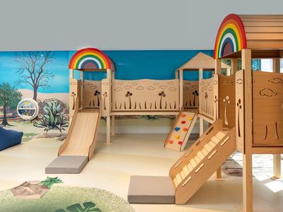 Área de juegos infantil interior con estructuras de madera y decoración de arcoíris para huéspedes del hotel.