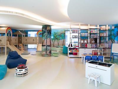Área de juegos infantil luminosa y amplia con mobiliario colorido y mural urbano en hotel.