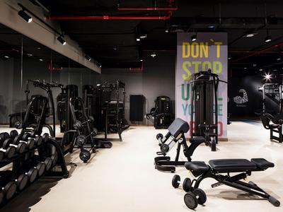 Gimnasio moderno con mancuernas, máquinas de entrenamiento y arte motivacional en la pared.