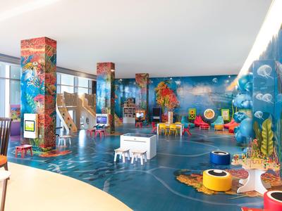 Zona de juegos colorida y espaciosa en hotel con murales marinos y mesas de juego.