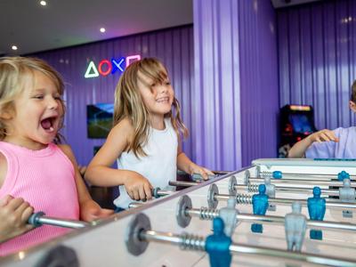 Tres niños juegan con entusiasmo al futbolín en una habitación moderna y colorida.