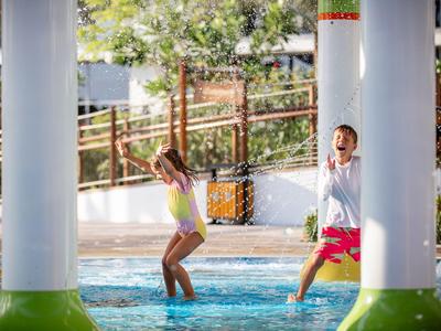 Niños juegan alegremente en el agua en un resort vacacional con decoración verde y blanca.
