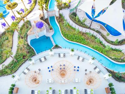 Vista aérea de una piscina en un resort con toboganes, tumbonas y áreas verdes.