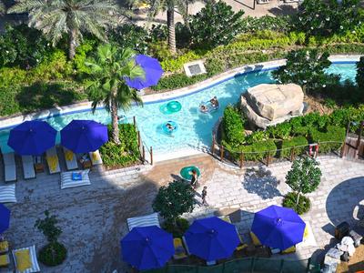 Vista de un área de piscina de hotel con sombrillas azules y entorno verde.