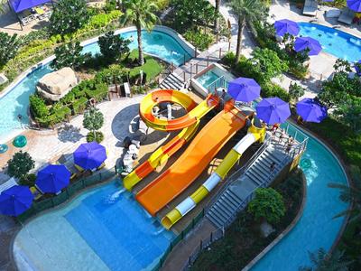 Toboganes de agua y piscinas con sombrillas azules en un resort tropical.