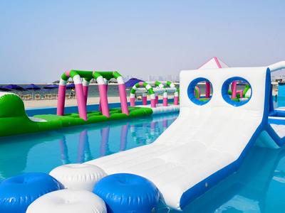 Parque acuático inflable con toboganes y obstáculos en una piscina azul clara.