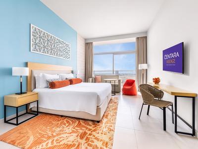 Habitación de hotel moderna con pared azul, cama doble, escritorio y vista a la ciudad.