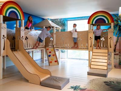 Área de juegos interior con tobogán, estructura para trepar y arcoíris coloridos para niños en un hotel.