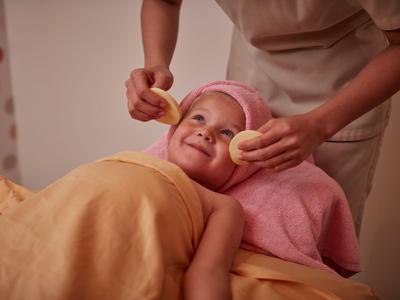 Un niño recibe un tratamiento facial relajante en un spa con tonos cálidos.