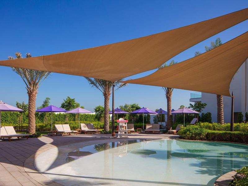 Zwembad met zonneschermen, ligstoelen en paarse parasols onder een heldere lucht.