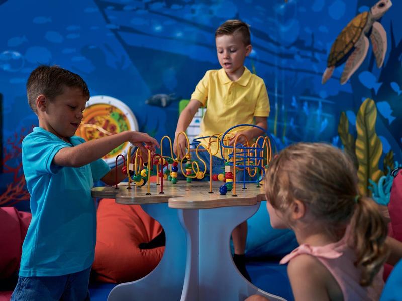 Kinderen spelen met een houten kralenspel in een kleurrijke onderwaterkamer met zitzakken.