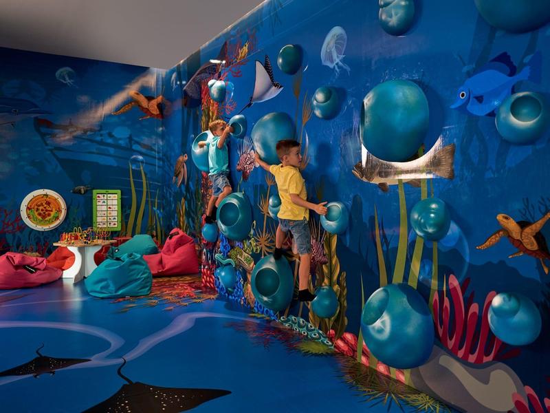 Kleurrijke onderwater-speelkamerwand met zeedieren en kinderen die klimmen en spelen.
