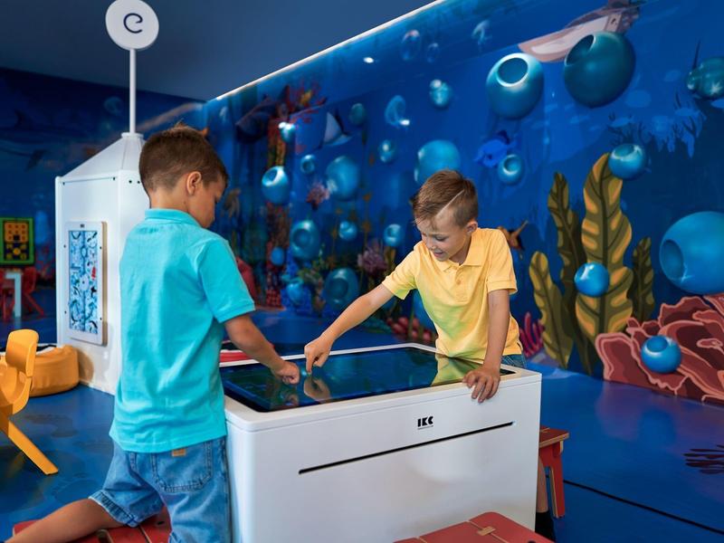 Kinderen spelen aan een interactieve tafel in een kleurrijke speelkamer met onderwaterthema.