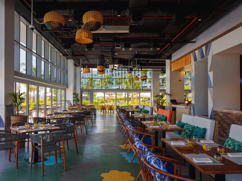 Modern restaurant met grote ramen, kleurrijke stoelen en een gezellige sfeer.