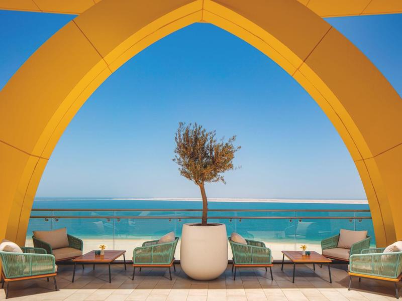 Terras met moderne zitmeubels en een boom in een grote witte pot met uitzicht op zee.