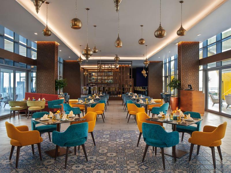 Modern restaurant met kleurrijke stoelen en grote ramen die gasten uitnodigen om in een hotel te eten.