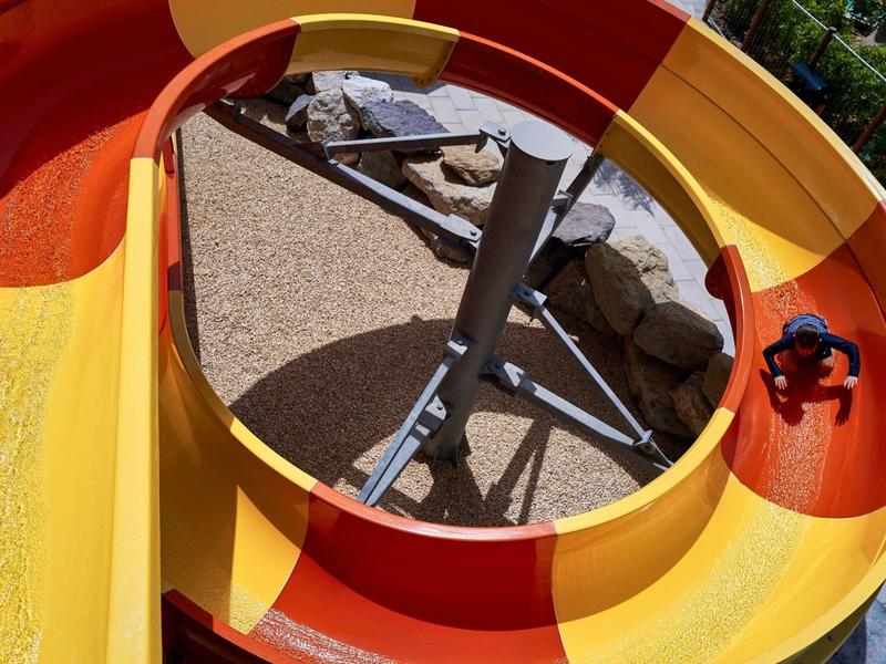 Gezicht door een ronde opening van een rode en gele glijbaan die de glijbaan en rotsen eronder toont.