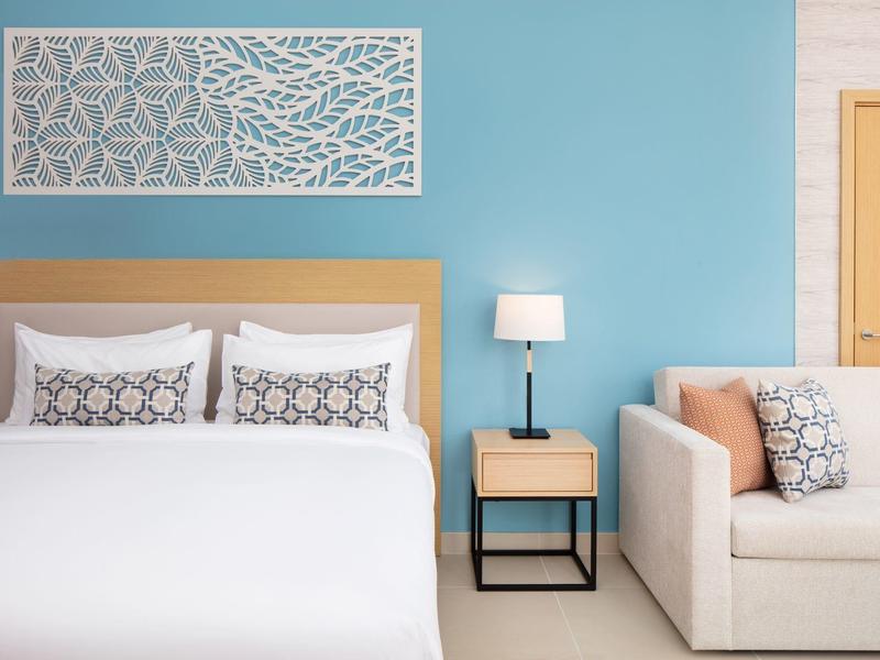 Lichte hotelkamer met blauw geschilderde muur, tweepersoonsbed, nachtkastje en bank.