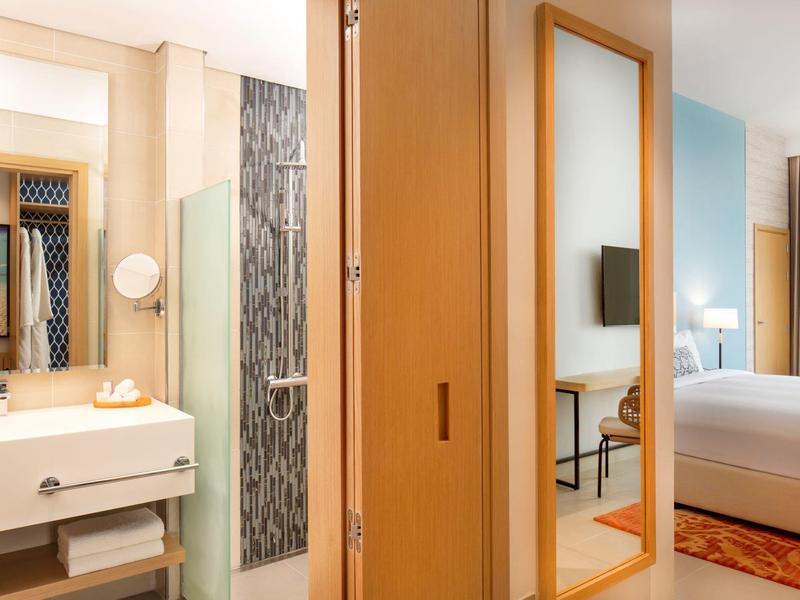 Modern hotelkamer met tweepersoonsbed, grote spiegel en lichte badkamerinrichting.