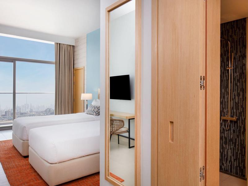 Lichte hotelkamer met bedden, groot raam en houten deur met spiegel