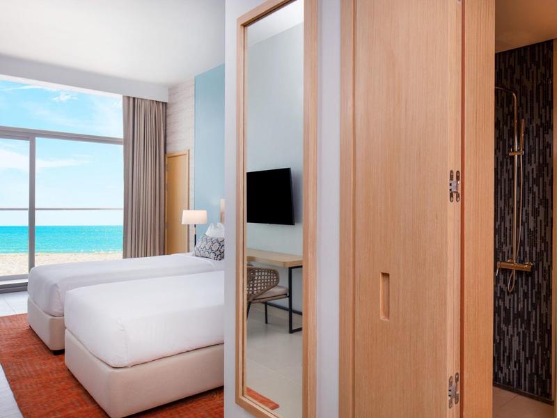 Lichte hotelkamer met twee bedden, groot raam en uitzicht op zee.