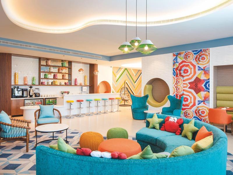 Kleurrijke hotel lounge met moderne zitplaatsen, bar en decoratieve muurschilderingen.