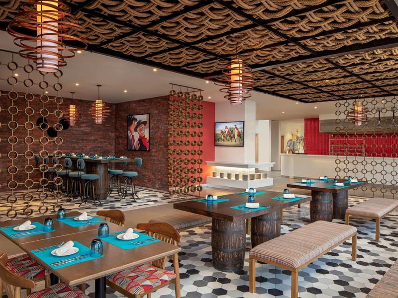 Modern restaurant met kleurrijke patronen, houten tafels en decoratieve lampen.