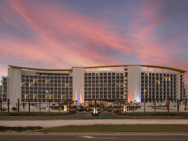 Modern hotelgebouw met veel ramen bij zonsondergang onder een roze-oranje lucht.