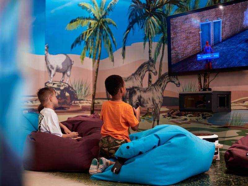 Twee jongens spelen videogames op een tv in een kleurrijke speelkamer met woestijnthema.