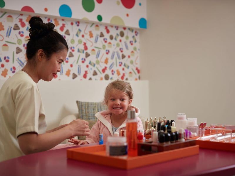 Kinderoppas die de nagels van een meisje schildert in een vriendelijke omgeving.