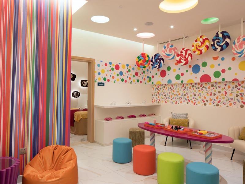 Kleurrijke speelkamer met krukjes, zitzakken en wanddecoratie in snoepstijl.