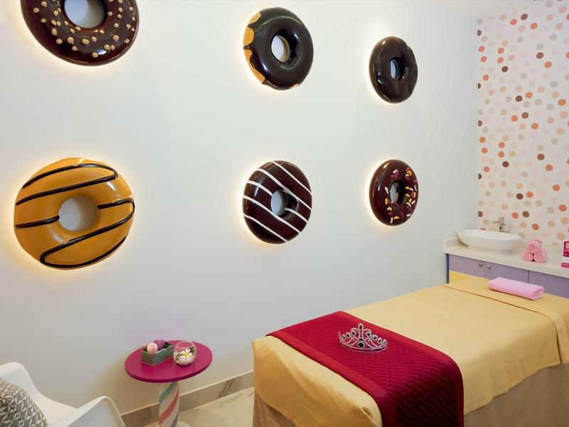 Behandelkamer met decoratieve donut muurschilderingen en massagetafel met rode loper