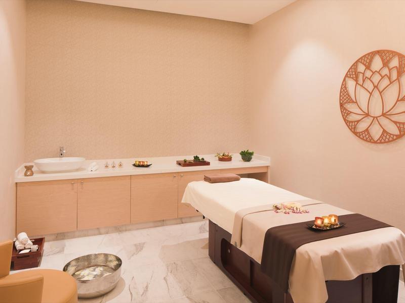 Lichte wellnessruimte met massagetafel, houten kast en decoratieve wandkunst.