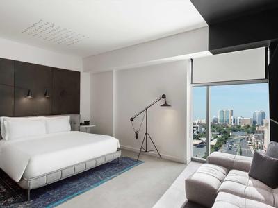 Modern hotel room with large bed, couch, and city view through the window.