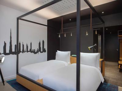 Modern hotel room with canopy bed, white bedding, and city skyline wall decor.
