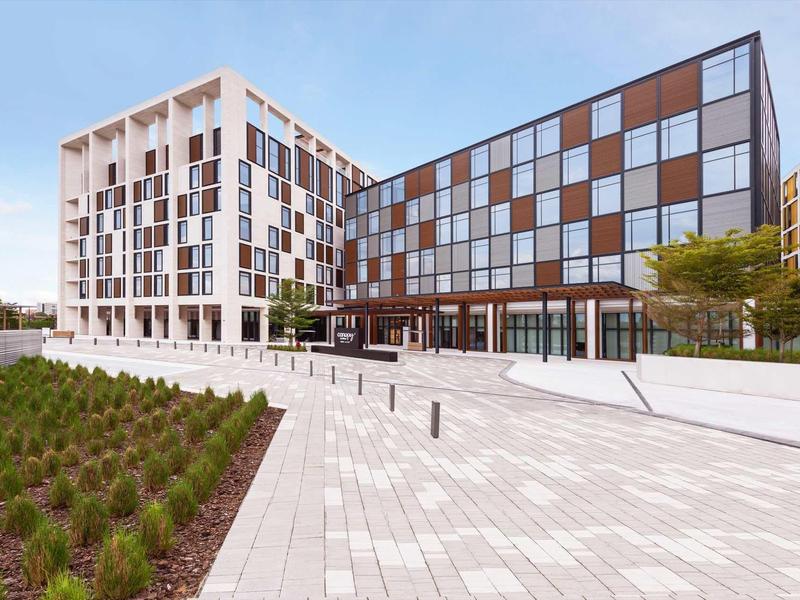 Modern hotel building with large glass facade and paved forecourt with plants