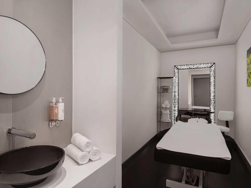 Modern wellness room with massage table, mirror, and sink in neutral tones.