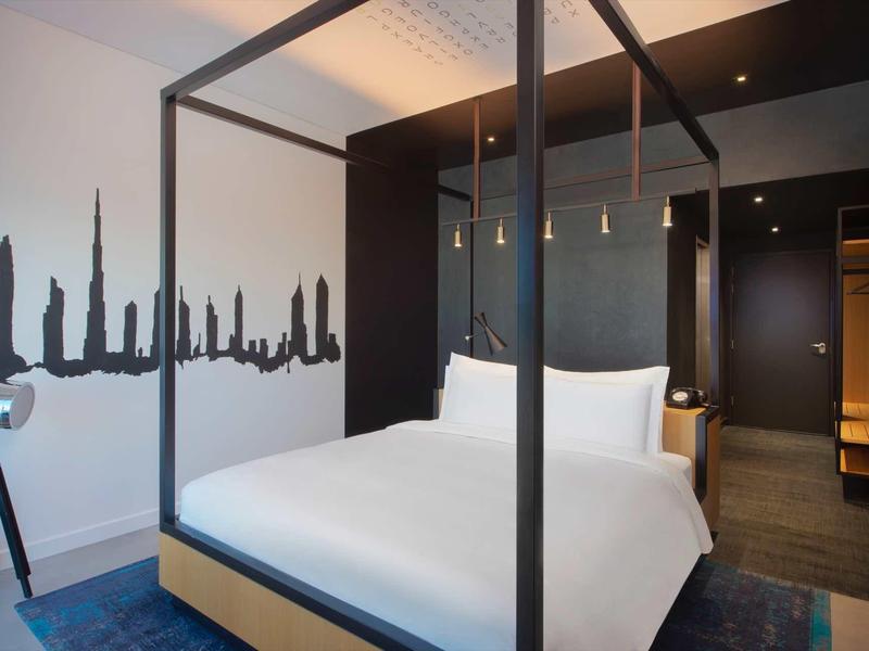 Modern hotel room with canopy bed, dark accent wall, and urban wall art.