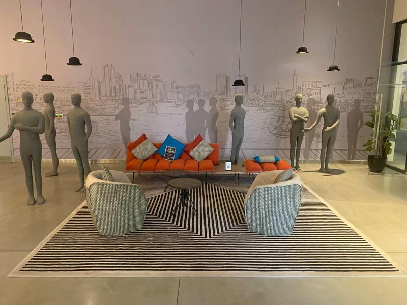 Modern hotel lounge area featuring sculptures, seating, and colorful cushions on a rug.