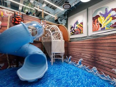 Innenraum mit blauem Spiraltunnelrutsche auf blauem Wasserboden und bunten Wandbildern.