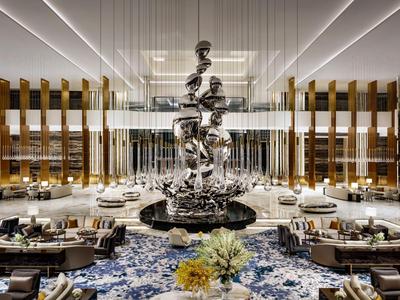 Duży, luksusowy hol hotelowy z nowoczesną rzeźbą i eleganckim rozmieszczeniem miejsc do siedzenia.