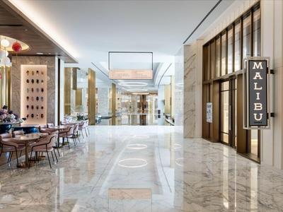 Jasny korytarz hotelowy z marmurową podłogą, stylowymi miejscami do siedzenia i restauracją Malibu.