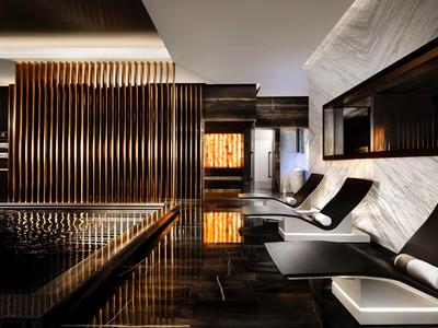 Moderner Wellnessraum mit dunklem Holz, Marmorwänden und weißen Liegen mit schwarzen Kissen.