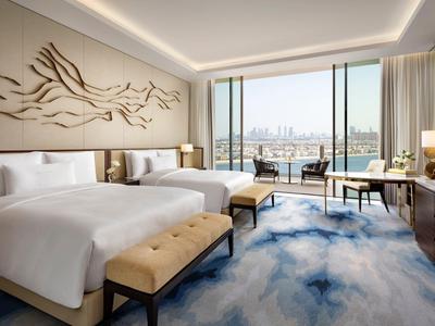 Modernes Hotelzimmer mit zwei Queensize-Betten, bodentiefen Fenstern und Stadtblick.