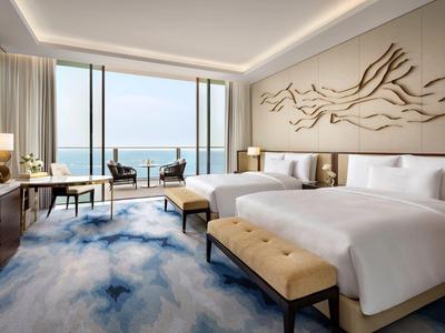 Modernes Hotelzimmer mit zwei Betten, bodentiefen Fenstern und Meerblick.